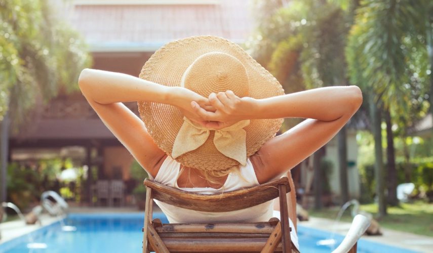 young women enjoying her holiday abroad. sat by the swimming pool, wearing a straw hat