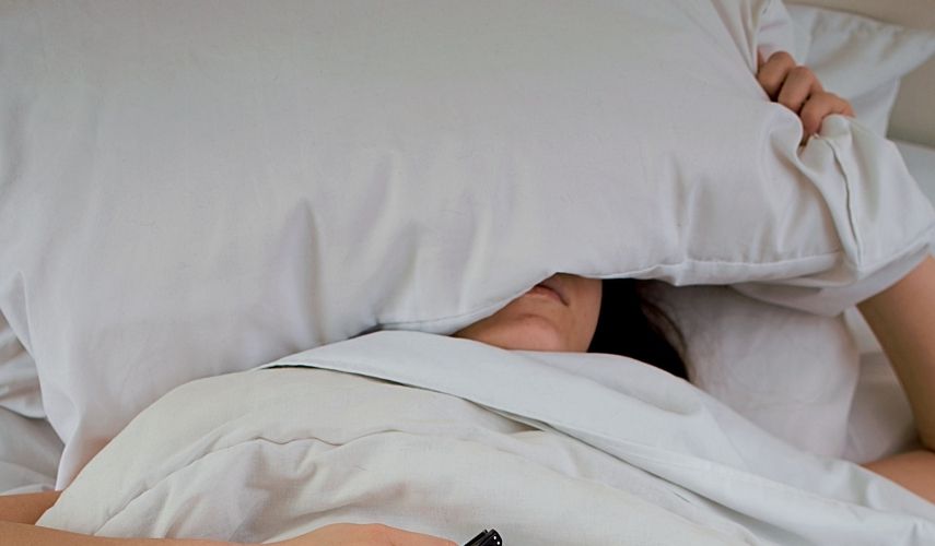 sleeping women in a white bed with a pillow over her head