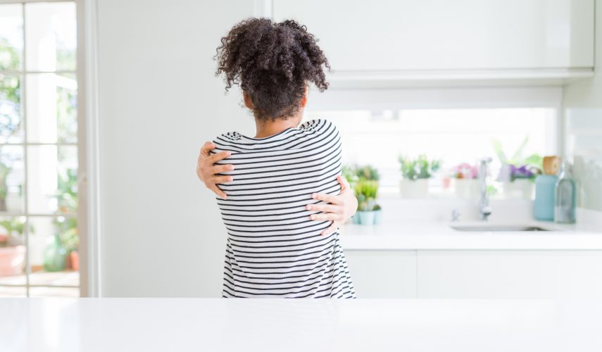 Beautiful african american woman with afro hair wearing casual striped sweater Hugging oneself happy and positive from backwards. Self love and self care